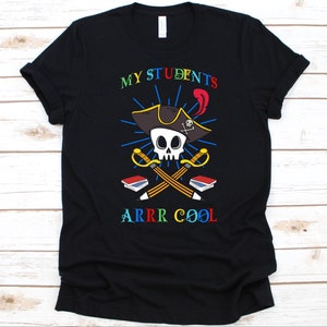 May include: Black t-shirt with a colorful graphic. The design features a skull wearing a pirate hat, crossed pencils and swords, and the text "MY STUDENTS ARRR COOL" in rainbow colors. The shirt is made of a soft material.