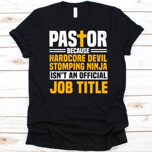 Puede incluir: Camiseta negra con la palabra "PASTOR" encima de un gráfico de cruz. Debajo, la camiseta dice "BECAUSE HARDCORE DEVIL STOMPING NINJA ISN'T AN OFFICIAL JOB TITLE" en letras blancas y amarillas.