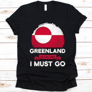 Może przedstawiać: Czarna koszulka z postarzanym wzorem flagi Grenlandii w kolorze czerwonym i białym. Tekst "GREENLAND IS CALLING I MUST GO" jest wydrukowany pod flagą na biało. Swobodny t-shirt dla miłośników Grenlandii.