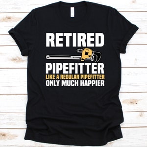 以下が含まれることがあります： 黒いTシャツ。白い文字で「RETIRED PIPEFITTER LIKE A REGULAR PIPEFITTER ONLY MUCH HAPPIER」と書かれています。「RETIRED」の下には、黄色と銀色のパイプレンチのグラフィックがあります。