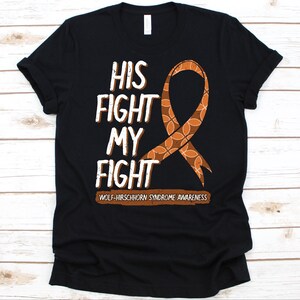 May include: Black t-shirt with the text "HIS FIGHT MY FIGHT" in white and brown. A brown and orange ribbon graphic is featured on the right side. The text "WOLF-HIRSCHHORN SYNDROME AWARENESS" is at the bottom.