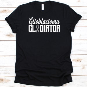 May include: Black t-shirt featuring the text "Glioblastoma GLADIATOR" in white, with a grey ribbon graphic. The shirt has a crew neck and is made of a soft material. The text is in a bold, easy-to-read font.