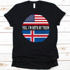 May include: Black t-shirt featuring a circular design with the American and Icelandic flags. The text "YES, I'M BOTH OF THEM" is centered within the design. The shirt is made of a soft material.