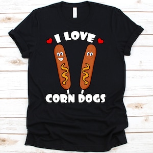 May include: Black t-shirt with the text "I LOVE CORN DOGS" in white. The design features two cartoon corn dogs with smiling faces and yellow mustard. Red hearts are above the corn dogs.