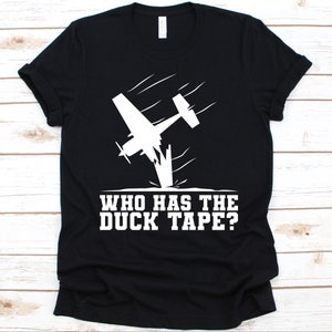 May include: Black t-shirt featuring a white graphic of a crashing airplane with the text "WHO HAS THE DUCK TAPE?" The design is a humorous take on aviation and repair.