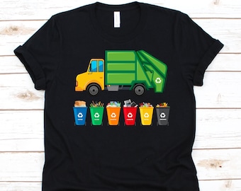 May include: Black t-shirt featuring a colorful illustration of a yellow and green garbage truck. Below the truck are six recycling bins in different colors, each labeled with a type of recyclable material. The design is centered on the shirt.