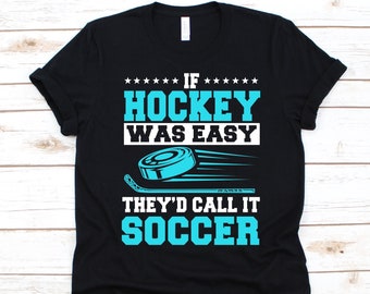 May include: Black t-shirt with a teal and white graphic. The graphic includes the text "IF HOCKEY WAS EASY THEY'D CALL IT SOCCER" along with a hockey puck and stick. The shirt is made of a soft material.
