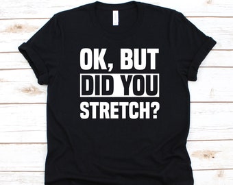 May include: Black t-shirt with the text "OK, BUT DID YOU STRETCH?" in white block letters. The text is centered on the shirt. The shirt has short sleeves and a crew neck.