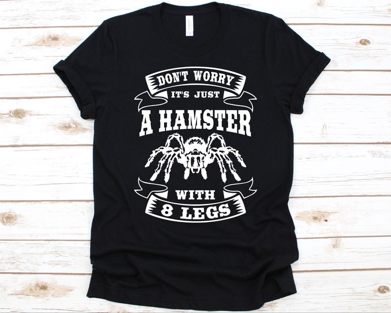 K&ouml;nnte beinhalten: Schwarzes T-Shirt mit wei&szlig;em Text und einer Vogelspinnen-Grafik. Der Text lautet "DON'T WORRY IT'S JUST A HAMSTER WITH 8 LEGS". Das Shirt besteht aus einem weichen Material.