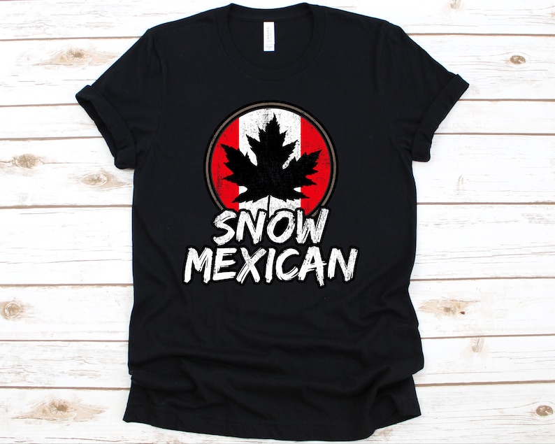 Pode incluir: Camiseta preta com um design circular com uma folha de bordo preta sobre um fundo vermelho e branco. O texto "SNOW MEXICAN" est&aacute; impresso em branco abaixo.