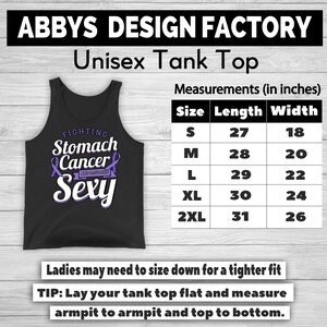 Op de afbeelding: Zwart unisex tanktop met de tekst "FIGHTING Stomach Cancer AND STILL THIS Sexy" in wit en paars. Afmetingen in centimeters, van S (68,5 cm lang, 45,7 cm breed) tot 2XL (78,7 cm lang, 66 cm breed).