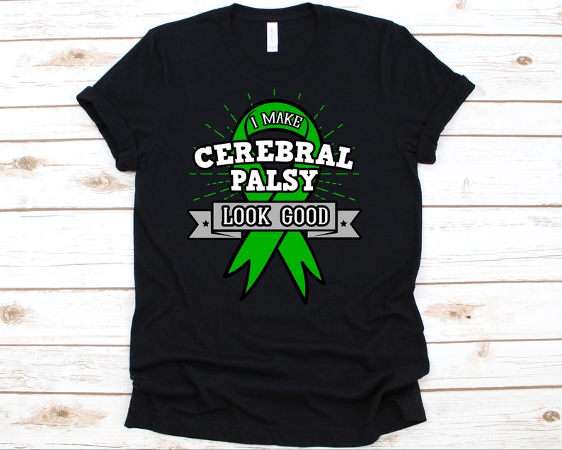 May include: Black t-shirt with a green ribbon design and the text "I MAKE CEREBRAL PALSY LOOK GOOD". The design includes white text and a gray banner. The shirt is made of a soft material.