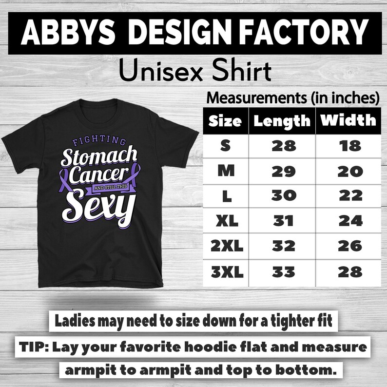 Op de afbeelding: Zwart unisex T-shirt met de tekst "FIGHTING Stomach Cancer AND STILL Sexy" in wit en paars. De maattabel toont de afmetingen in inches, vari&euml;rend van maat S tot 3XL. Het shirt is van Abbys Design Factory.