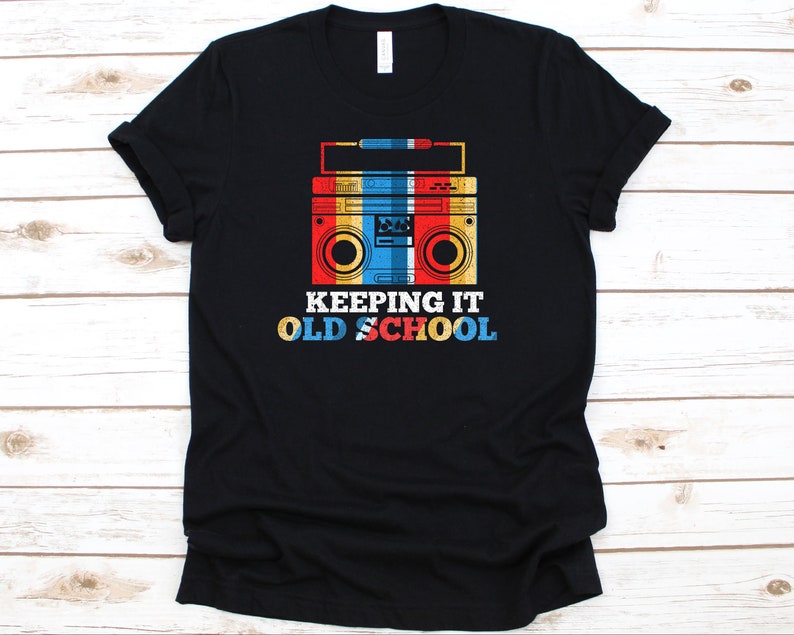 May include: Black t-shirt featuring a retro boombox graphic in red, yellow, blue, and white. The text "KEEPING IT OLD SCHOOL" is below the boombox. A classic design for music lovers.