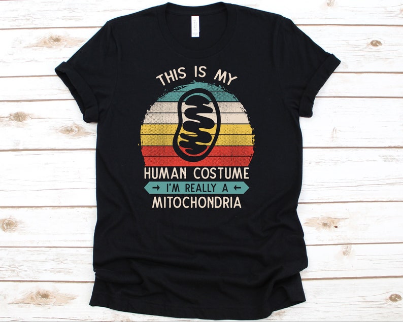 May include: Black t-shirt with a retro design. The design features a mitochondria illustration inside a circle with the text "THIS IS MY HUMAN COSTUME I'M REALLY A MITOCHONDRIA". The design has a vintage color scheme.