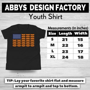 May include: Black youth shirt featuring a design of the American flag made of hot dogs. The shirt includes a size chart with measurements in inches. The text "ABBYS DESIGN FACTORY Youth Shirt" is at the top.