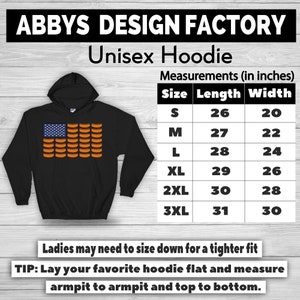 May include: Black unisex hoodie with a graphic of an American flag made of hot dogs. The hoodie has a hood and a size chart with measurements in inches. The text "ABBYS DESIGN FACTORY" and "Unisex Hoodie" are at the top.