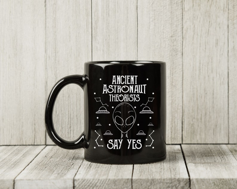 Puede incluir: Taza de cer&aacute;mica negra con el texto blanco "ANCIENT ASTRONAUT THEORISTS SAY YES". El dise&ntilde;o incluye una cara alien&iacute;gena, constelaciones y platillos volantes. La taza tiene un asa curva.