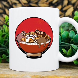 May include: White ceramic mug featuring a cartoon illustration of sloths lounging in a bowl of ramen noodles. The ramen bowl is red and brown, set against a red circle. The mug has a white handle and is perfect for coffee, tea, or any beverage.