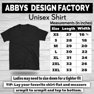 May include: A black unisex t-shirt from Abbys Design Factory. The shirt sizes range from XS to 3XL, with lengths from 27 to 33 inches and widths from 16.5 to 28 inches. The image includes a size chart and instructions for measuring a shirt.