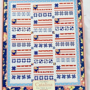 Può includere: Un kit per trapunte con un design patriottico, con strisce rosse e bianche, stelle blu e accenti floreali. La trapunta ha uno sfondo bianco ed è incorniciata da un bordo floreale. Il kit include il testo "Catalina" e "Fig Tree & Co."