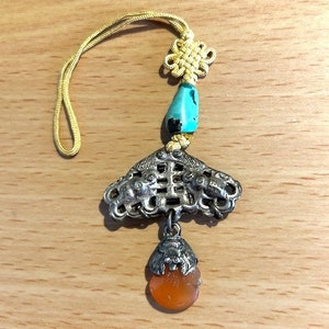 May include: A silver charm with a turquoise bead and an orange bead. The charm is in the shape of a four-leaf clover with a decorative design. The charm is attached to a yellow cord.