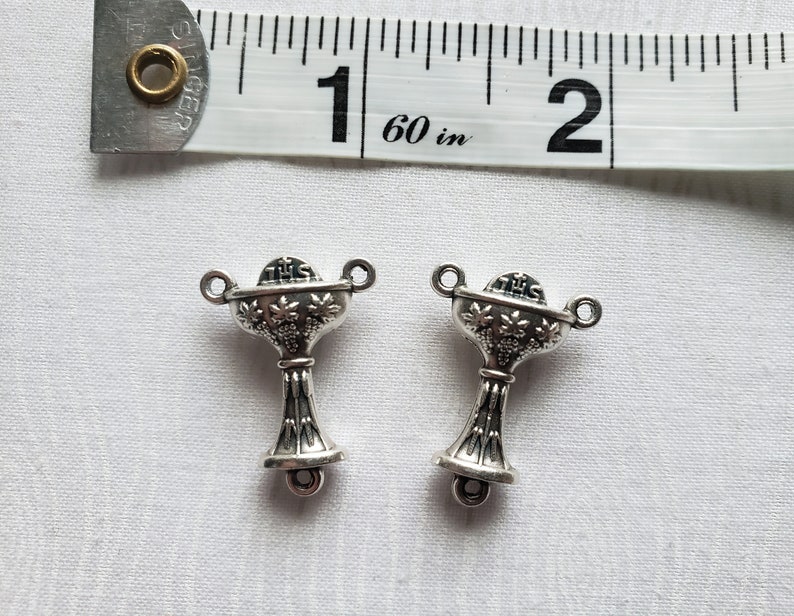 Pu&ograve; includere: Due ciondoli d'argento a forma di calice con un motivo a vite e le parole "Questo &egrave; il mio corpo" sul davanti. I ciondoli misurano circa 2,5 cm di lunghezza.