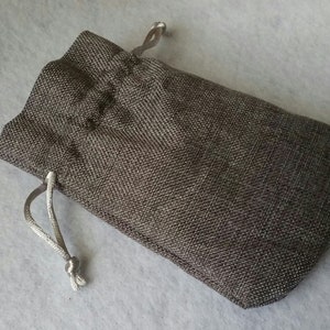 Pu&ograve; includere: Una piccola borsa a cordoncino grigia realizzata in tessuto strutturato. La borsa ha un cordoncino bianco.