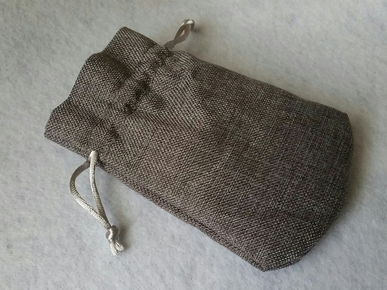 Pu&ograve; includere: Una piccola borsa a cordoncino grigia realizzata in tessuto strutturato. La borsa ha un cordoncino bianco.