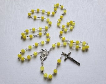 May include: A rosary with yellow beads and a silver crucifix. The beads are round and evenly spaced, connected by a silver chain. The crucifix is a simple cross design.