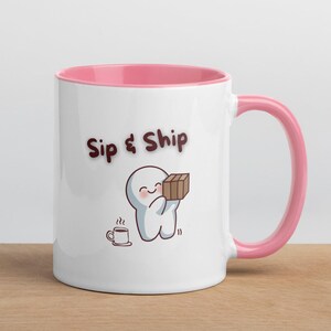 Könnte beinhalten: Weiße Keramiktasse mit rosa Innenraum und Henkel. Die Tasse trägt den Text "Sip & Ship" und eine Cartoonfigur, die ein Paket hält. Eine kleine Tasse Kaffee ist ebenfalls abgebildet. Die Tasse steht auf einer Holzoberfläche.