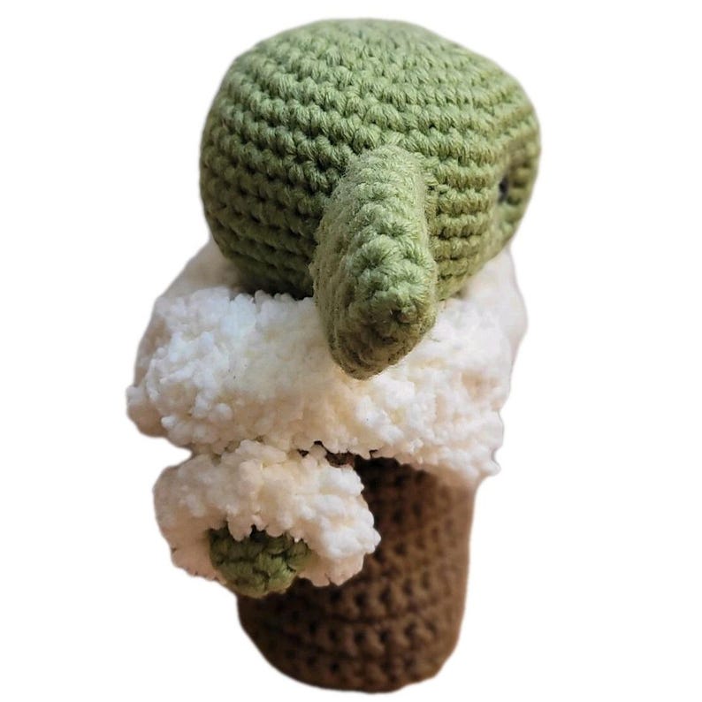 May include: A handmade crochet doll in the likeness of a popular character. The doll features a green head and ears, a white fluffy collar, and a brown base. The doll is made of soft yarn and is a unique, handcrafted item.