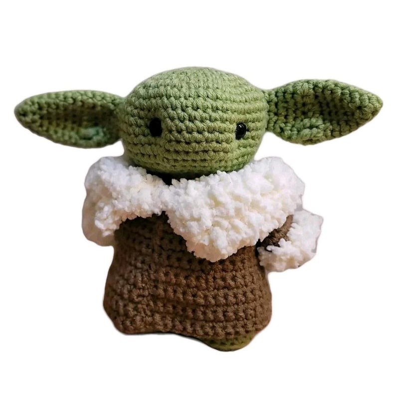 May include: A crocheted doll of a character with large ears, a green head, and a brown body. The doll has black eyes and a white fluffy collar. The doll is handmade and appears to be a character from a popular science fiction franchise.