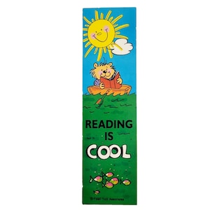 May include: A colorful bookmark featuring a cartoon bear reading a book in a boat under a smiling sun. The text "READING IS COOL" is displayed on a green background with fish illustrations. A fun and educational item.