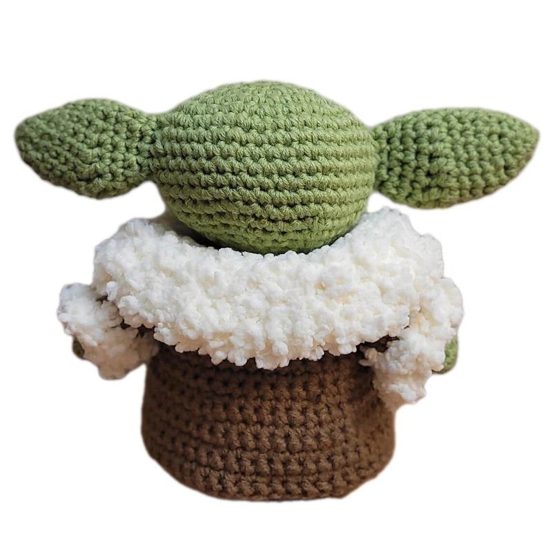 May include: A handmade crochet doll in the likeness of a popular character. The doll features a green head and large ears, a white fluffy collar, and a brown body. The doll is made with a textured stitch.