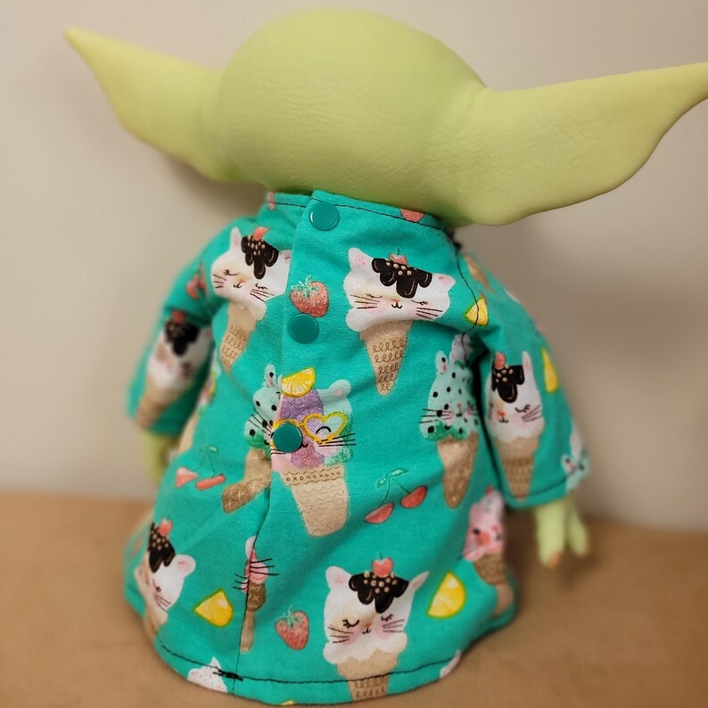 May include: A green plush figure wearing a button-up shirt with an ice cream cone and cat pattern. The shirt has a teal background with illustrations of ice cream cones, cats, strawberries, and lemons.