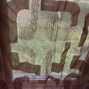 May include: A sheer brown curtain with a large, abstract design. The curtain is made of a lightweight fabric, allowing light to filter through. The design appears to be a series of overlapping shapes, creating a modern aesthetic. The background shows a blurred outdoor scene.