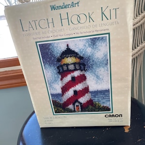 May include: Latch hook kit for a red and white lighthouse with a blue sky and ocean background. The kit is by WonderArt and includes Caron yarn. The kit is 15 inches by 20 inches.
