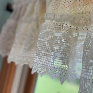 May include: White crocheted lace valance with a scalloped edge. The lace is delicate and intricate, with a repeating pattern of small squares.