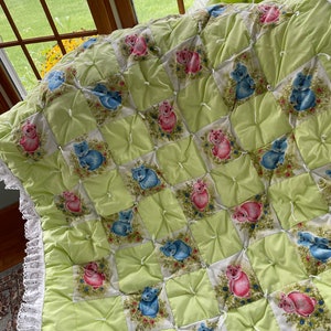 May include: A green and white quilted baby blanket with a checkered pattern and embroidered bears. The blanket has a white lace trim.