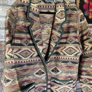 May include: A green, brown, and beige patterned blazer with a green trim and two pockets. The blazer has a button closure and a label that reads "Casually".