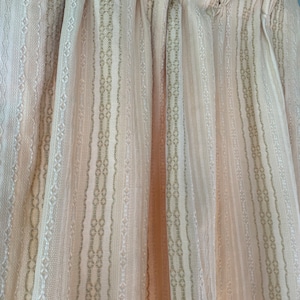 May include: A pair of sheer curtains with a delicate pattern of vertical stripes in a light pink and beige color.