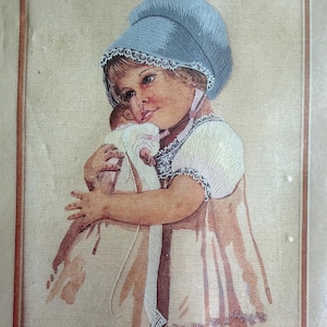 May include: Embroidered artwork of a young child in a blue bonnet, embracing a doll. The artwork features a soft color palette with a beige background and a brown frame. The child's dress has a pink and white design.