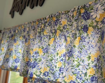 May include: A floral valance with a blue and yellow floral pattern. The valance is hung above a window with a wooden frame. The word "farmhouse" is written in black on the wall above the valance.