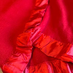 May include: Close-up of a vibrant red fabric with a contrasting satin trim. The fabric appears to be a soft material, possibly wool or a similar textile. The satin trim adds a touch of elegance and texture to the design.