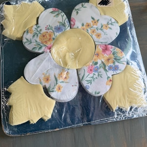 May include: A set of floral heart-shaped coasters and leaf-shaped coasters, packaged in clear plastic. The coasters feature a white background with a floral pattern in yellow, pink, and blue. The leaf coasters are yellow.