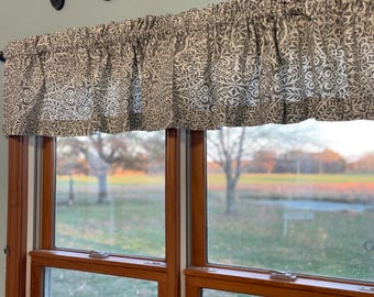 May include: A valance with a gray and white floral pattern hangs above a wooden window. The word "farmhouse" is spelled out in dark brown letters above the valance. The window looks out onto a grassy field.