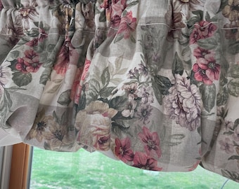 May include: A beige and white valance with a floral pattern featuring pink, green, and brown flowers. The valance has a ruffled edge and a checkered pattern.