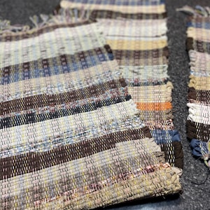May include: Three woven rugs with a brown, blue, and beige striped pattern. The rugs have fringe on the ends.