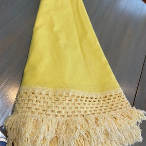 May include: A yellow tablecloth with a crocheted lace trim and fringe. The tablecloth is made of a smooth, silky fabric.